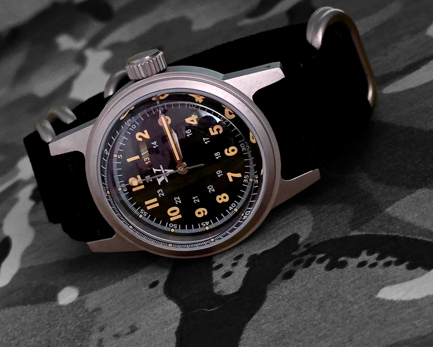 The NORMANDY Field Watch 3 6mm by Five Minutes Before features an NH35 automatic movement and boasts a vintage design with a black dial, yellow numerals, and camouflage fabric. It has a silver case, black strap, silver hands, and a prominent crown on the side.