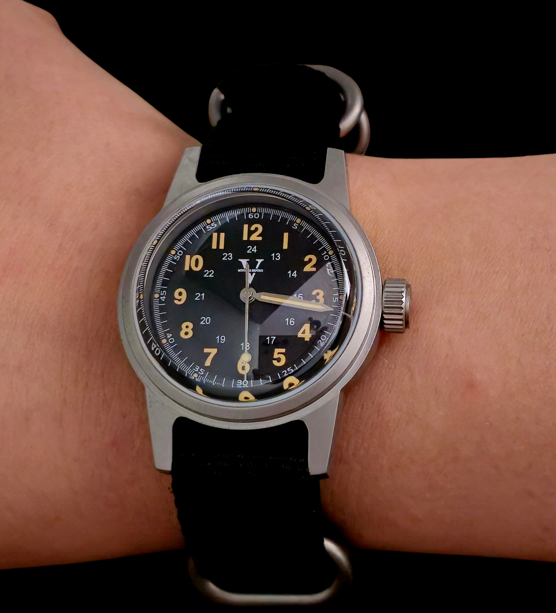 The NORMANDY by Five Minutes Before is a 36mm field watch with a black dial, yellow hour markers, white minute markers, and a 24-hour scale. Silver hands glide over the face powered by an NH35 automatic movement, completed with a black fabric strap for rugged charm.