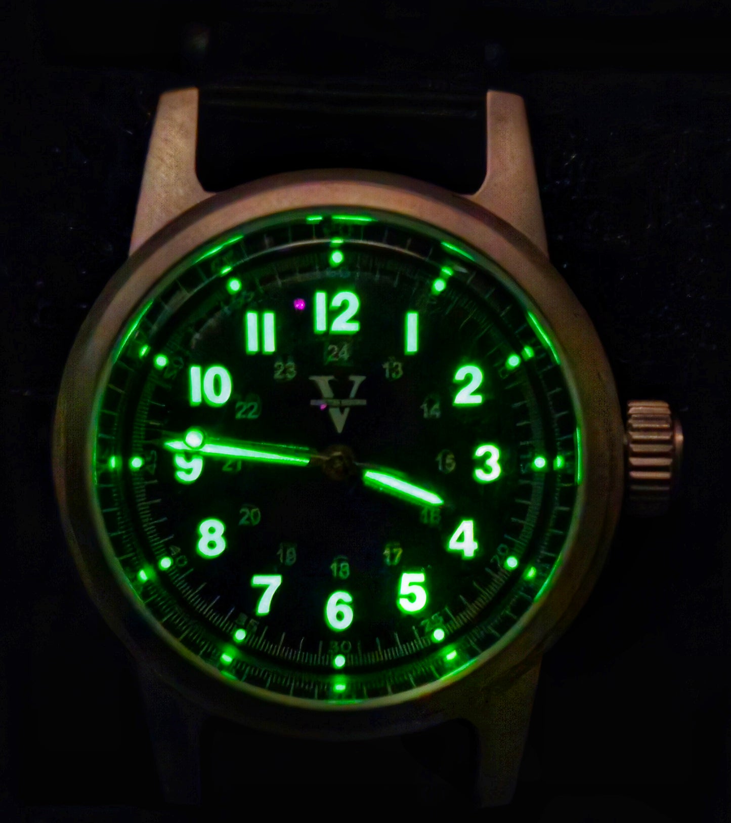 The NORMANDY (Field watch 36mm) by Five Minutes Before features an NH35 automatic movement, displaying 10:09. It has a dark dial with green glowing numbers and hands. Its metallic finish case, with a right-side crown, epitomizes the rugged elegance of field watches.
