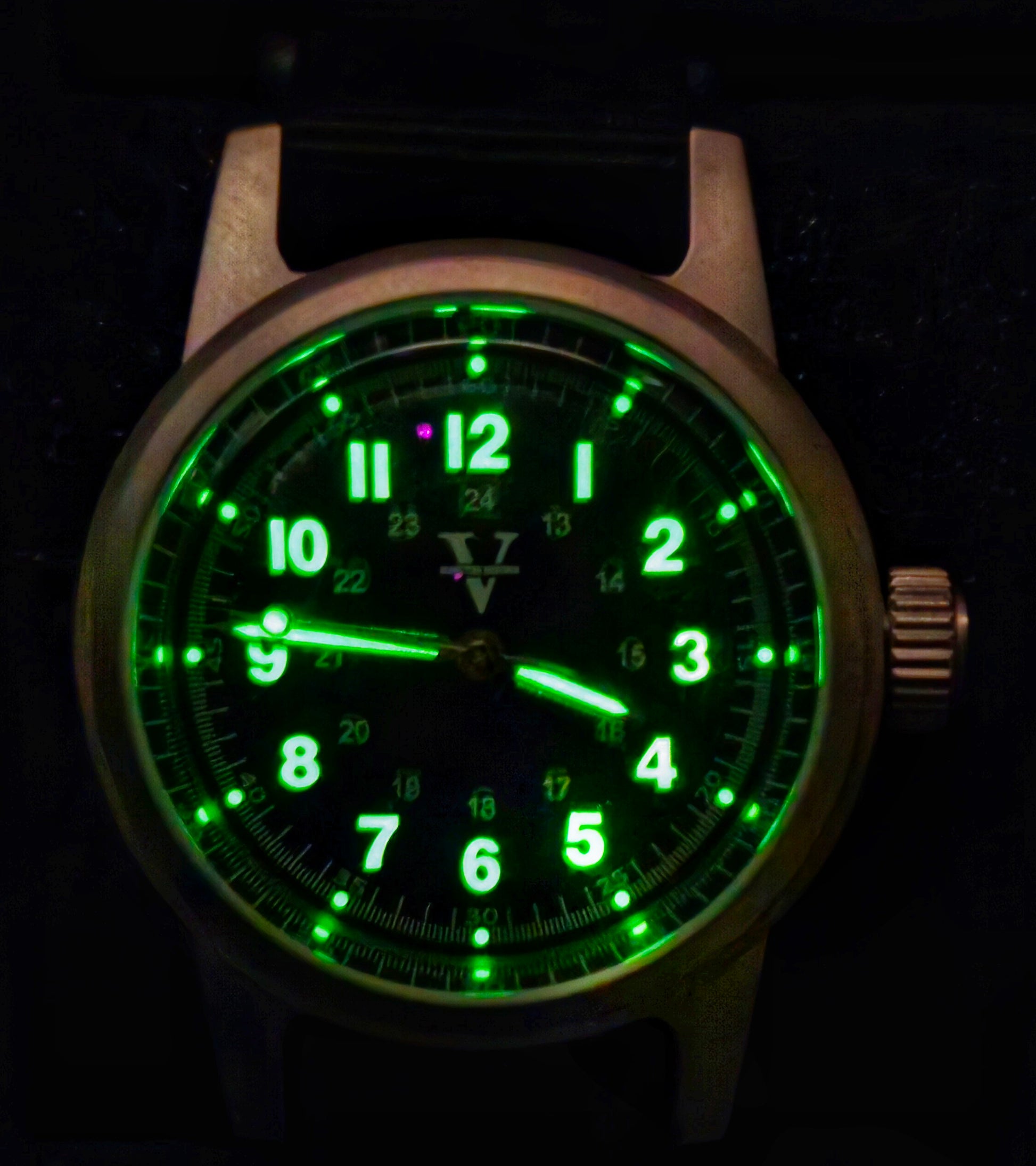 The NORMANDY (Field watch 36mm) by Five Minutes Before features an NH35 automatic movement, displaying 10:09. It has a dark dial with green glowing numbers and hands. Its metallic finish case, with a right-side crown, epitomizes the rugged elegance of field watches.