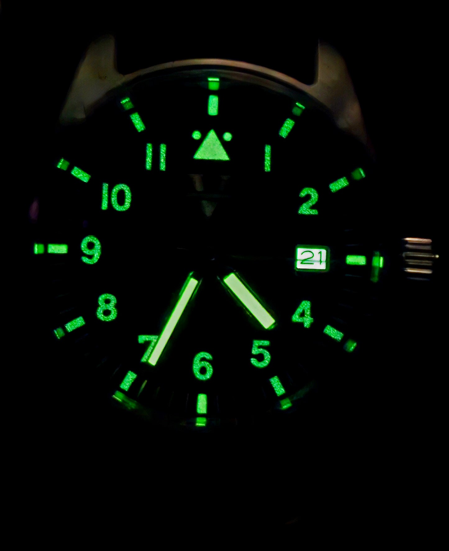 In the dark, a VANGUARD field watch by Five Minutes Before emits a luminous glow; green numerals and hands show the time as around 5:25. Its housed in a 39mm stainless steel case with a date window displaying 21.