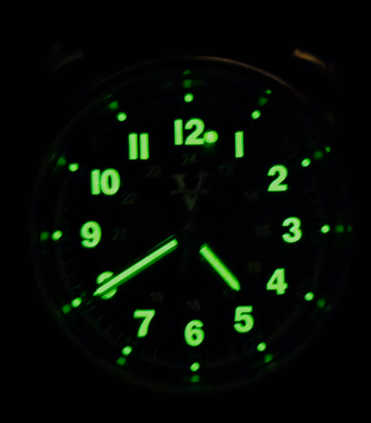 In the shadowy darkness, the Five Minutes Before ECLIPSE Field Watch (36mm) reveals glowing green numbers and hands on its stainless steel frame. The time shows around 5:11, with illuminated elements highlighting a clear, readable design reminiscent of an eclipse.