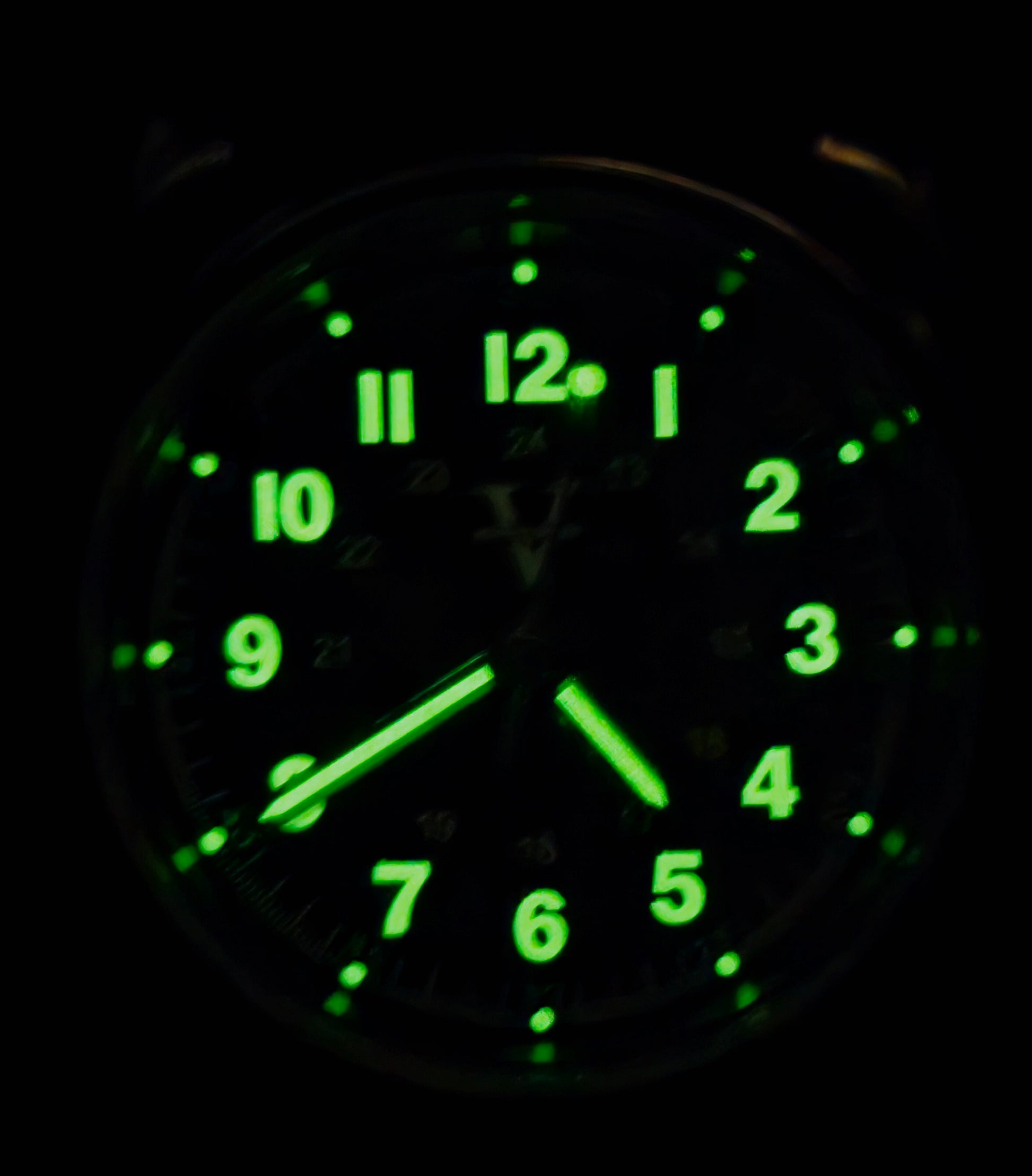 In the shadowy darkness, the Five Minutes Before ECLIPSE Field Watch (36mm) reveals glowing green numbers and hands on its stainless steel frame. The time shows around 5:11, with illuminated elements highlighting a clear, readable design reminiscent of an eclipse.